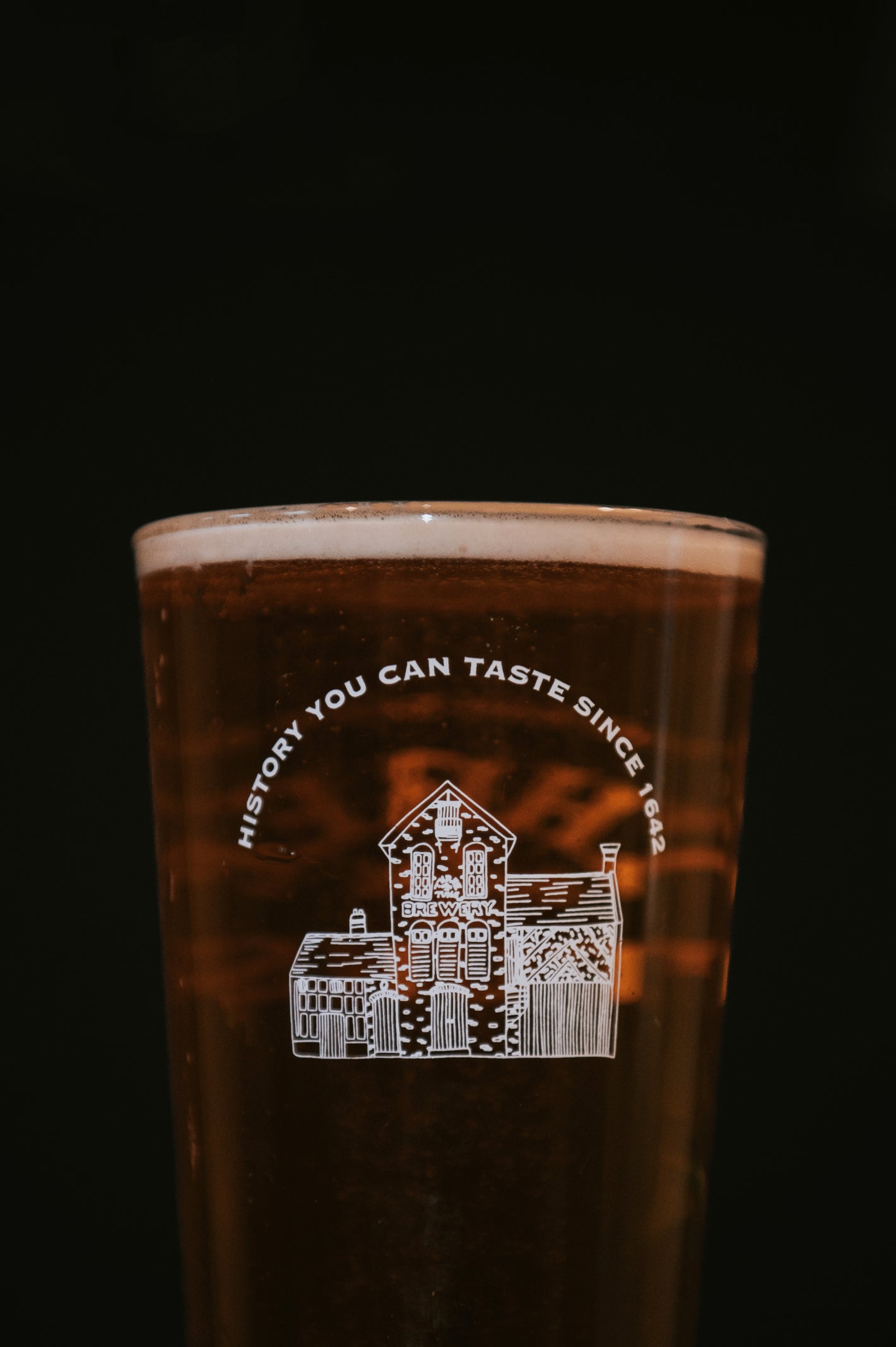 pint glass of beer with three tuns brewery logo and tagline on a black background