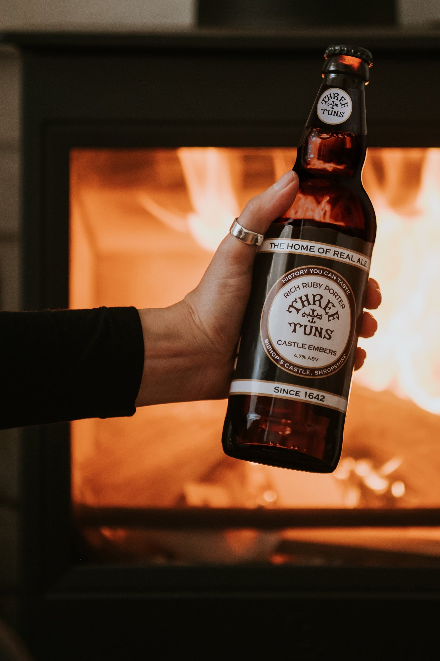person holding bottle of castle embers real ale three tuns brewery beer bottle in front of a fireplace