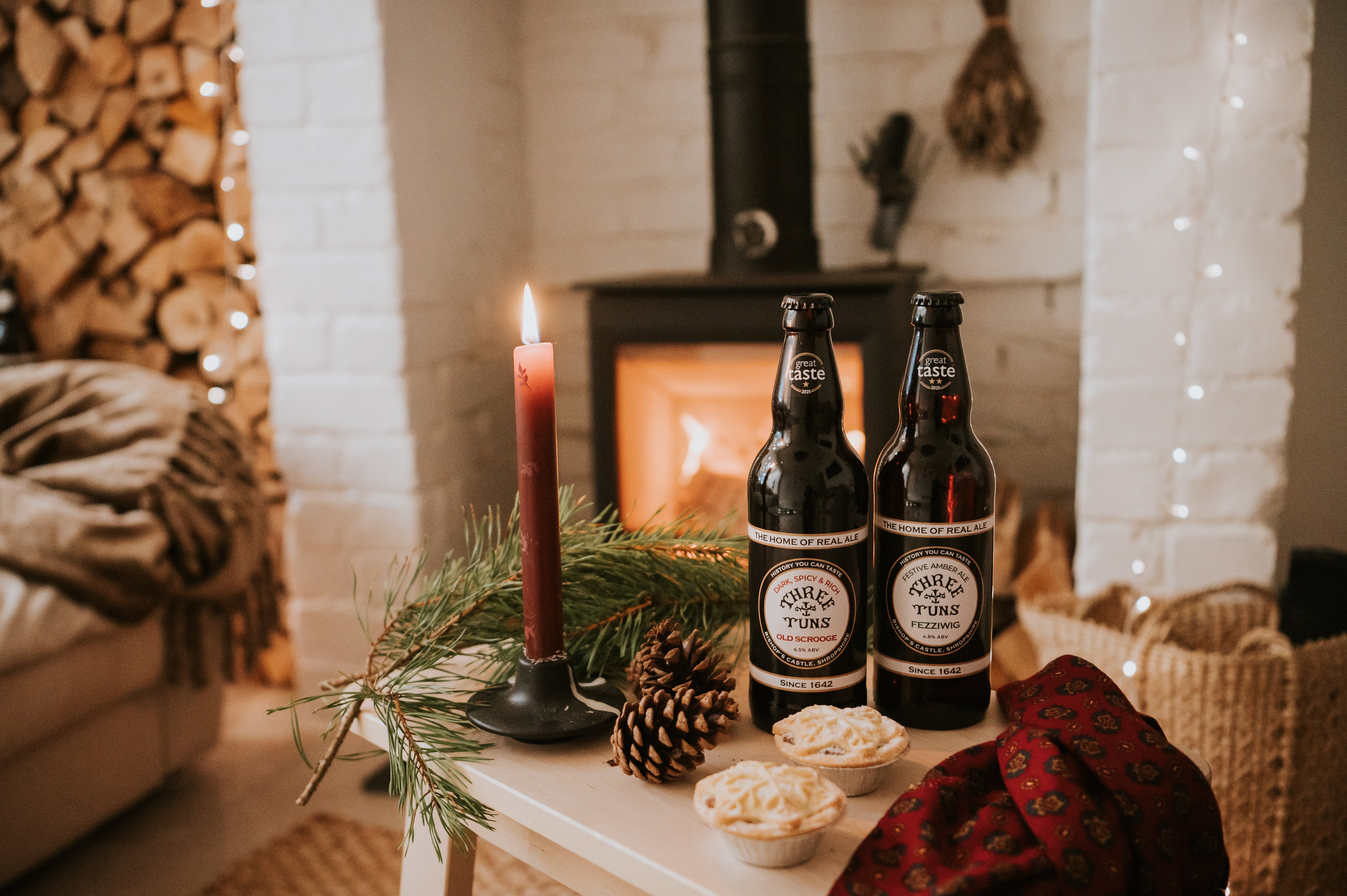 two bottles of three tuns brewery beer on a table in a cosy living room with a fireplace and christmas decorations